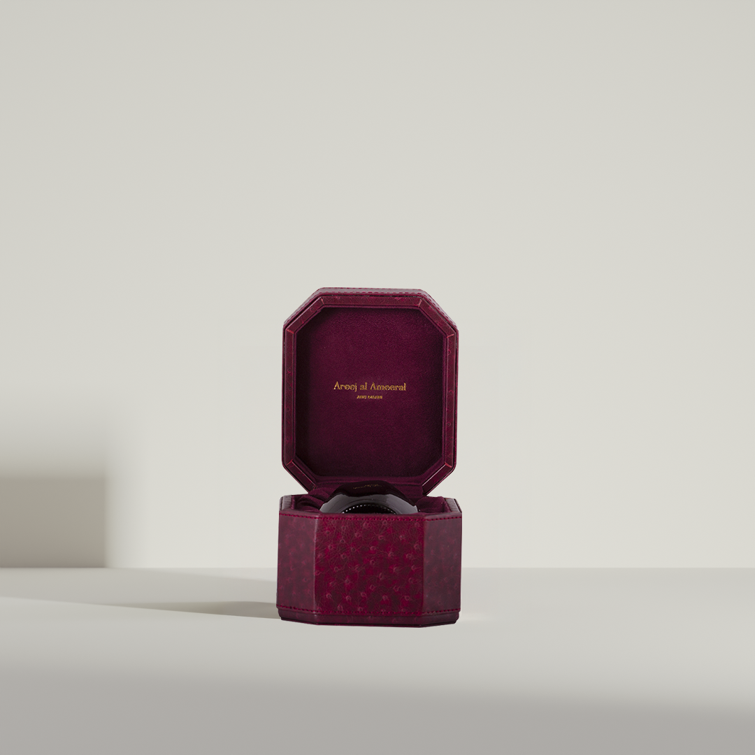 Colored glass jar with a label in a box, containing Oud_Mubakhar_Sultann, against a light background.